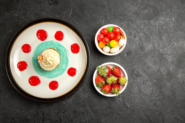 Bovenaanzicht van verre snoepjes op de tafel witte cupcake en kommen met snoep en aardbeien op de zwarte tafel