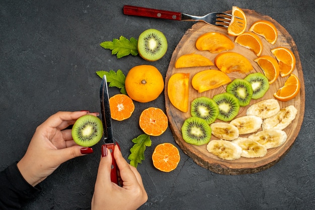 Bovenaanzicht van vers fruit op een houten dienblad, hand met een sinaasappel op een zwarte ondergrond