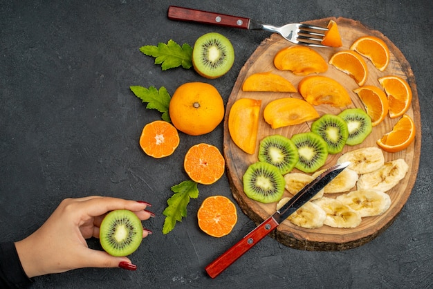 Bovenaanzicht van vers fruit op een houten dienblad, hand met een sinaasappel op zwarte tafel