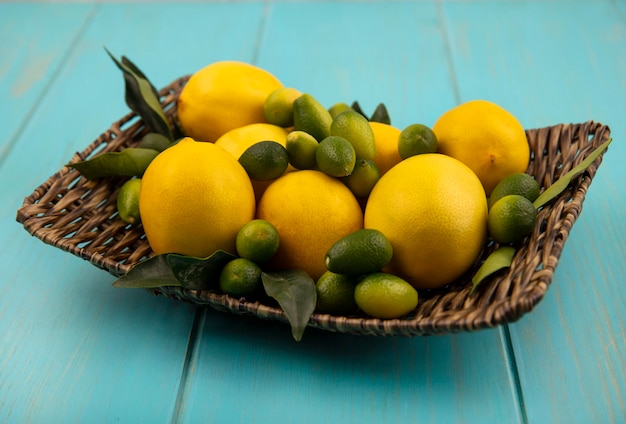 Bovenaanzicht van vers fruit zoals kinkans en citroenen op een rieten dienblad op een blauwe houten muur