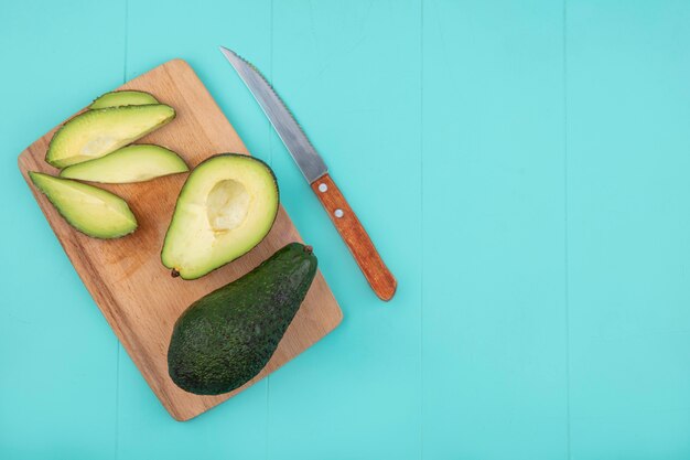 Bovenaanzicht van vers gesneden avocado met mes op houten keukenbord op blauw