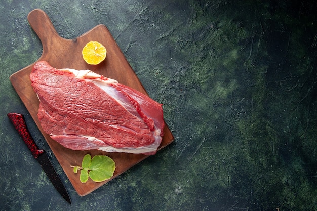 Bovenaanzicht van vers rauw rood vlees citroen op bruin houten snijplank en mes op donkere kleur achtergrond