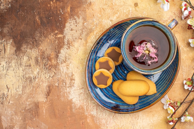 Bovenaanzicht van verschillende koekjes een kopje thee en bloemen op tafel met gemengde kleuren