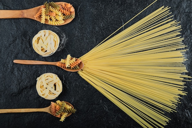 Bovenaanzicht van verschillende ongekookte pasta op donker.