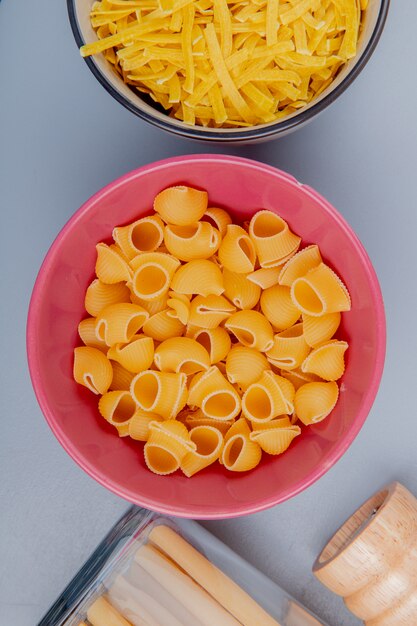 Bovenaanzicht van verschillende soorten pasta in kommen als pijp-rigate tagliatelle bucatini op blauwe ondergrond