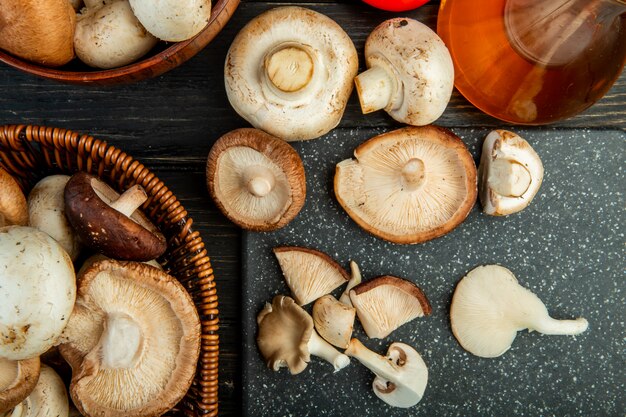 Bovenaanzicht van verse champignons in een rieten mand en op een zwarte snijplank op donker hout