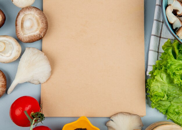 Bovenaanzicht van verse champignons met tomatensla gerangschikt rond een schetsboek op lichtblauw