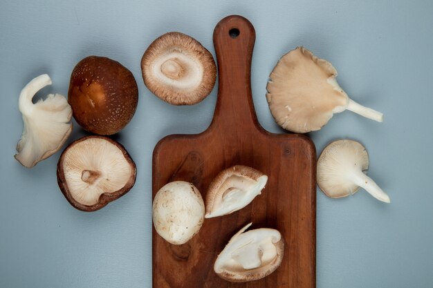 Bovenaanzicht van verse champignons op een houten snijplank op lichtblauw