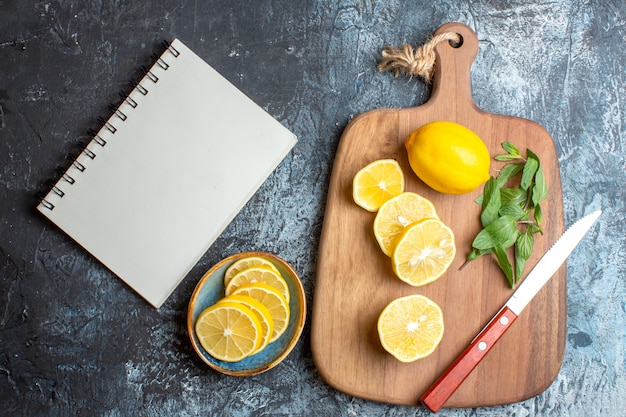 Gratis foto bovenaanzicht van verse citroenen en muntmes op een houten snijplank naast notebook op donkere achtergrond
