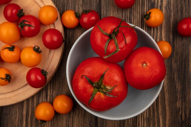 Bovenaanzicht van verse drie grote rode tomaten op een kom met kerstomaatjes geïsoleerd op een houten keukenbord op een houten oppervlak