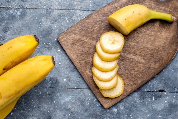 Bovenaanzicht van verse gele bananen gesneden en geheel op grijs