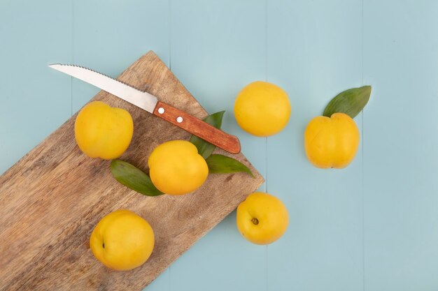 Bovenaanzicht van verse gele perziken geïsoleerd op een houten keukenbord met mes op een blauwe achtergrond