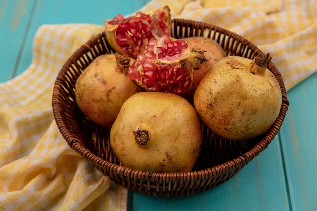 Bovenaanzicht van verse granaatappels op een emmer op een geel geruit doek op een blauwe houten ondergrond