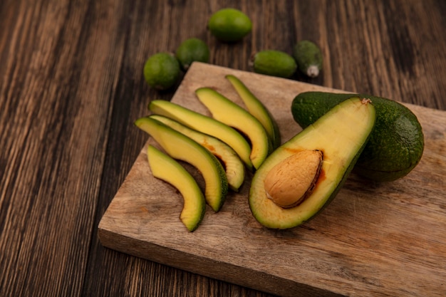 Bovenaanzicht van verse groene gevilde avocado's op een houten keukenbord met feijoas geïsoleerd op een houten achtergrond