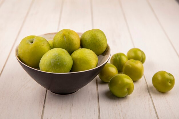 Bovenaanzicht van verse groene kersenpruimen op een zwarte kom met groene kersenpruimen geïsoleerd op een houten achtergrond