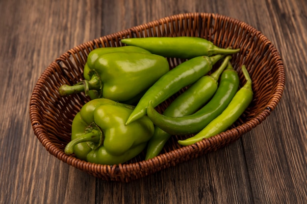 Gratis foto bovenaanzicht van verse groene paprika's op een emmer op een houten achtergrond