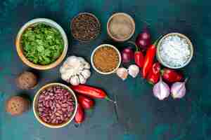 Gratis foto bovenaanzicht van verse groenten, uien, paprika, knoflook, greens en kruiderijen op donkerblauw bureau, plantaardige voedselmaaltijdpeper