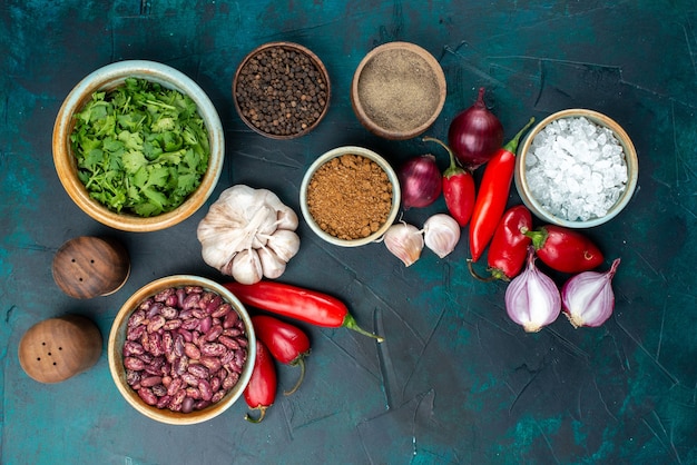 Bovenaanzicht van verse groenten, uien, paprika, knoflook, greens en kruiderijen op donkerblauw bureau, plantaardige voedselmaaltijdpeper