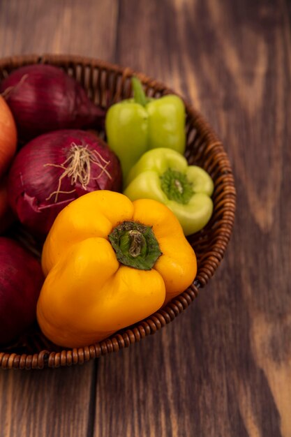 Bovenaanzicht van verse groenten zoals kleurrijke paprika's en uien op een emmer op een houten ondergrond