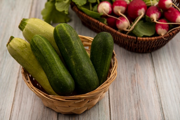 Bovenaanzicht van verse groenten zoals komkommers en courgettes op een emmer met radijs op een emmer op een grijze houten muur