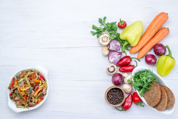 Bovenaanzicht van verse groenten zoals peperworteluien met broodbroodjes op licht bureau, plantaardige voedselmaaltijd vitamine