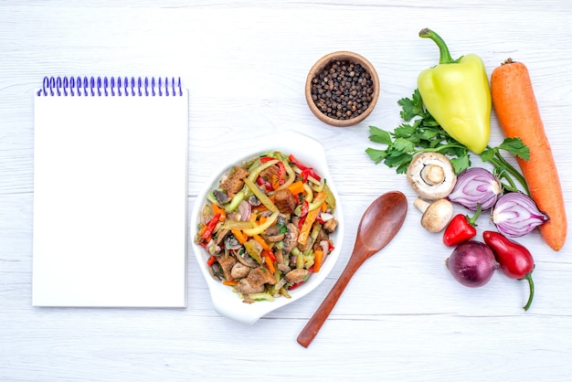 Bovenaanzicht van verse groenten zoals wortel uien greens en groene paprika met vleesplakken op licht, plantaardig voedsel maaltijd vitamine vlees