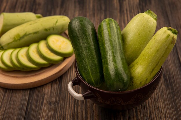 Bovenaanzicht van verse komkommers op een kom met gehakte courgettes op een houten keukenbord op een houten muur