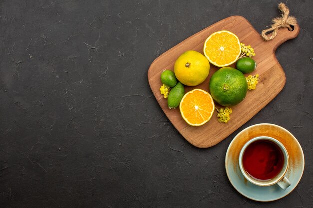 Bovenaanzicht van verse mandarijnen met feijoa en kopje thee op zwart