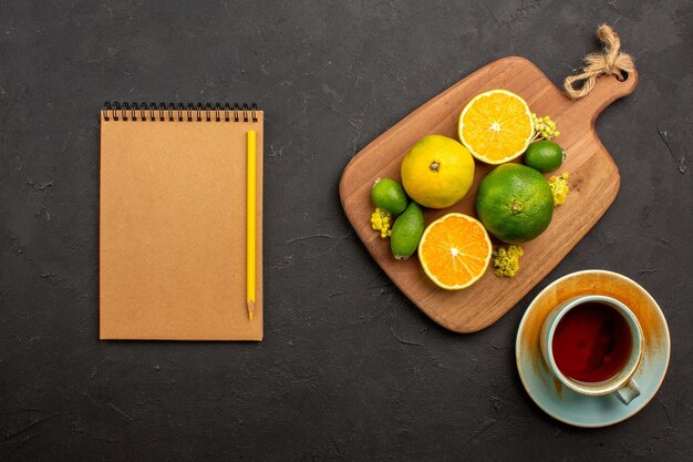 Bovenaanzicht van verse mandarijnen met feijoa en kopje thee op zwart