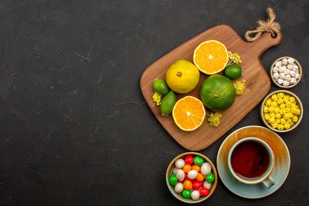 Bovenaanzicht van verse mandarijnen met kopje thee en snoep op zwart