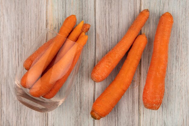 Bovenaanzicht van verse oranje wortelen op een glas met wortelen geïsoleerd op een grijze houten achtergrond