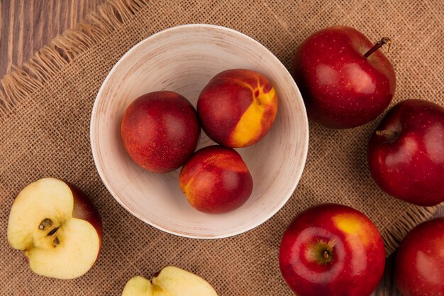 Bovenaanzicht van verse perziken op een kom op een zakdoek met appels geïsoleerd op een houten achtergrond