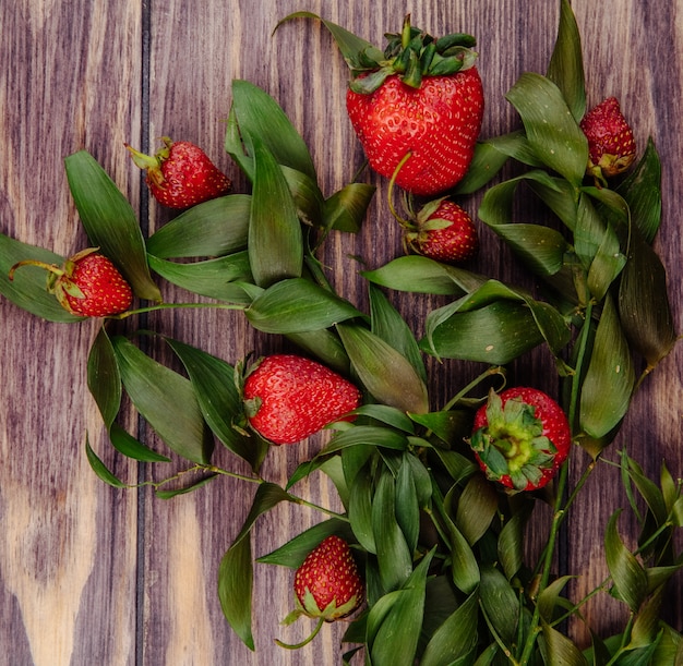 Gratis foto bovenaanzicht van verse rijpe aardbeien en groene bladeren op hout