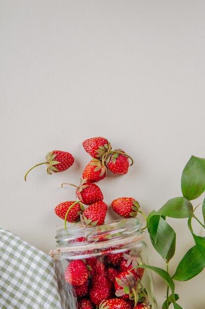 Bovenaanzicht van verse rijpe aardbeien verspreid uit glazen pot op wit