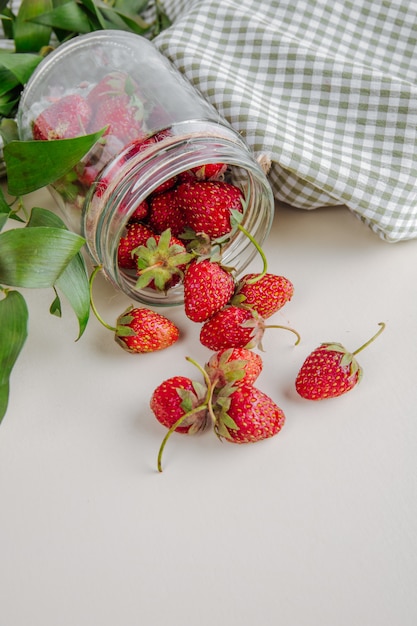 Bovenaanzicht van verse rijpe aardbeien verspreid uit glazen pot op wit