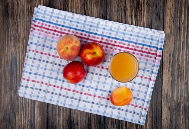 Bovenaanzicht van verse rijpe nectarines en perziken met een glas perziksap op plaidservet op rustiek hout