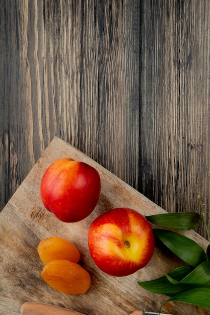 Bovenaanzicht van verse rijpe nectarines met gedroogde abrikozen op houten snijplank op rustieke achtergrond met kopie ruimte