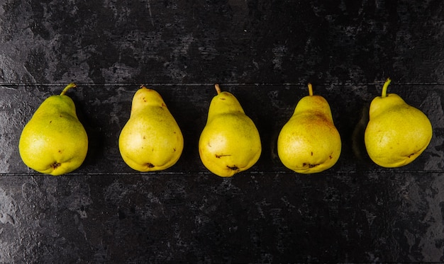 Bovenaanzicht van verse rijpe peren in een lijn op zwarte houten achtergrond met kopie ruimte