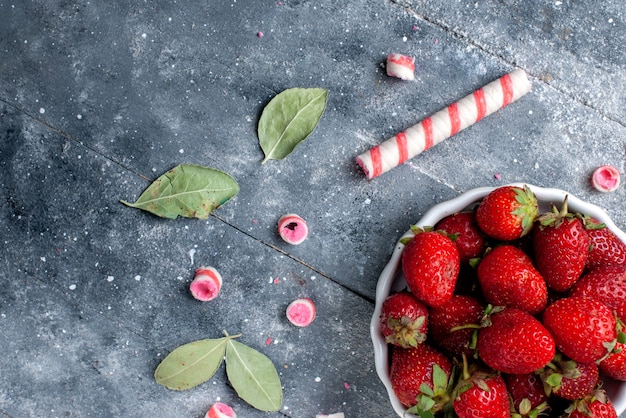 Bovenaanzicht van verse rode aardbeien in plaat samen met stok snoepjes op grijs, fruit bessen vers snoep zacht zoet