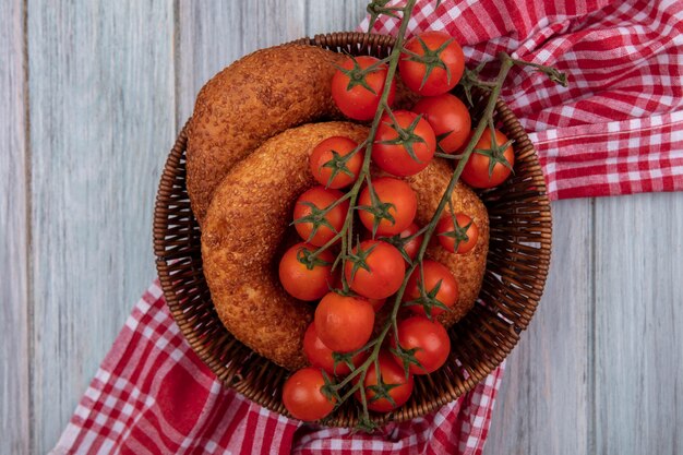 Bovenaanzicht van verse rode tomaten op een emmer met bagels op een zakdoek op een grijze houten achtergrond