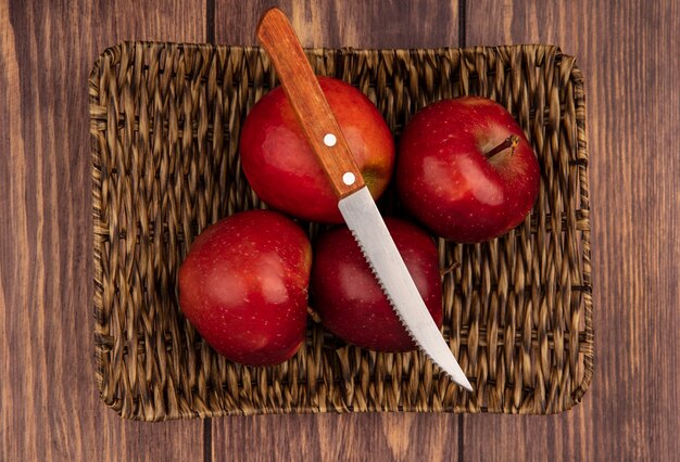 Bovenaanzicht van verse, sappige en rode appels op een rieten dienblad met mes op een houten achtergrond