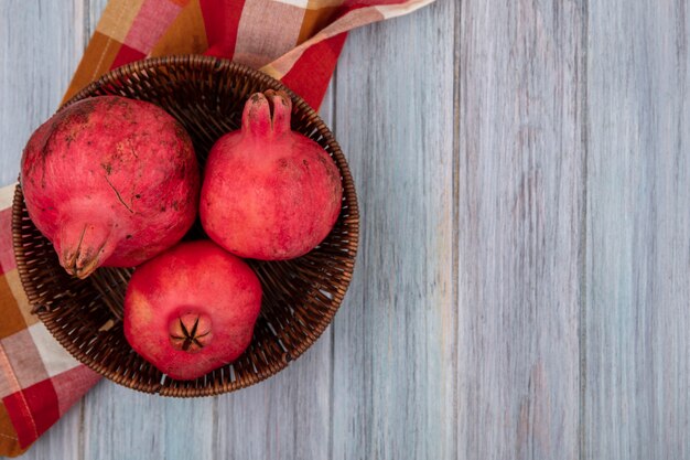 Bovenaanzicht van verse, sappige en rossige granaatappels op een emmer op een gecontroleerde doek op een grijze achtergrond met kopie ruimte