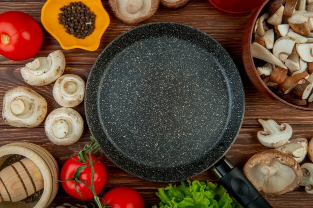 Bovenaanzicht van verse witte champignons met tomaten houten vijzel met gedroogde kruiden zwarte peperkorrels gerangschikt rond een koekenpan op rustieke houten tafel