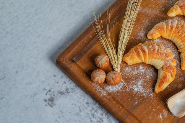 Bovenaanzicht van verse zelfgemaakte croissants op een houten bord over grijze ondergrond.