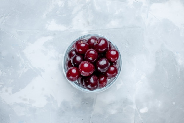 Bovenaanzicht van verse zure kersen in glazen beker op lichtwit bureau, fruit zure bes vitamine foto