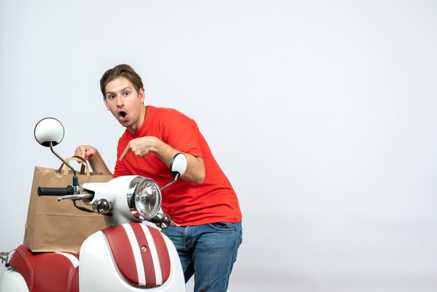 Bovenaanzicht van verwarde bezorger in rood uniform staande in de buurt van de bestelling van de scooter op witte achtergrond