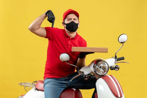 Bovenaanzicht van verwarde koerier man met rode blouse en hoed handschoenen in medische masker zittend op scooter naar beneden wijst en volgorde tonen