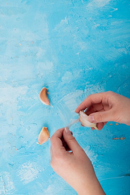 Bovenaanzicht van vrouw hand knoflook teentje peeling op blauwe achtergrond met kopie ruimte