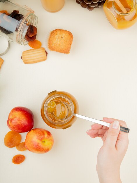 Bovenaanzicht van vrouw hand met glazen pot perzik jam met perziken rozijnen cupcake op witte ondergrond