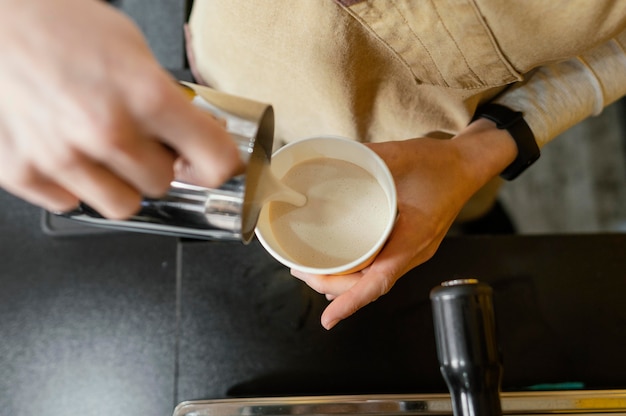 Bovenaanzicht van vrouwelijke barista gieten opgeschuimde melk in beker